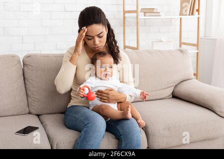 Mamma nera che ha mal di testa seduta con piangendo bambino a casa Foto Stock