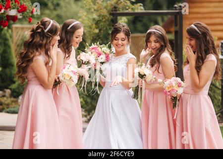 Buona sposa con bridesmaid tenere bouquet e divertirsi all'aperto. Bella bridesmaid negli stessi abiti stand vicino alla sposa affascinante in lungo abito da sposa Foto Stock