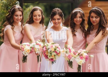 Buona sposa con bridesmaid tenere bouquet e divertirsi all'aperto. Bella bridesmaid negli stessi abiti stand vicino alla sposa affascinante in lungo abito da sposa Foto Stock