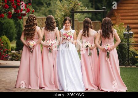 Buona sposa con bridesmaid tenere bouquet e divertirsi all'aperto. Bella bridesmaid negli stessi abiti stand vicino alla sposa affascinante in lungo abito da sposa Foto Stock