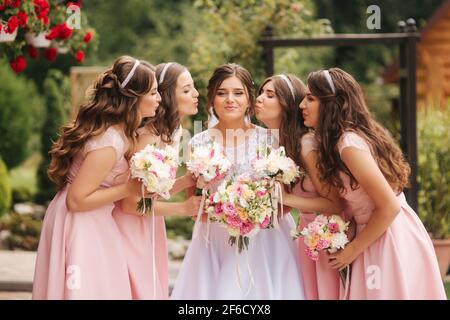 Buona sposa con bridesmaid tenere bouquet e divertirsi all'aperto. Bella bridesmaid negli stessi abiti stand vicino alla sposa affascinante in lungo abito da sposa Foto Stock