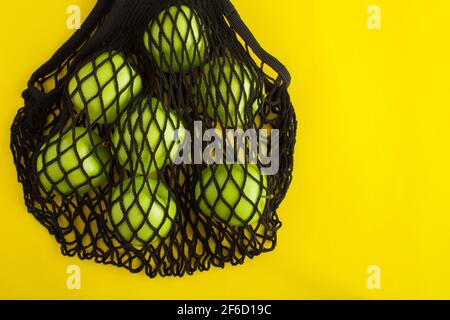 Nessun concetto di sacchetto di plastica. Borsa nera di shopping in mesh con mele verdi su sfondo giallo. Vista dall'alto. Spazio di copia. Foto Stock