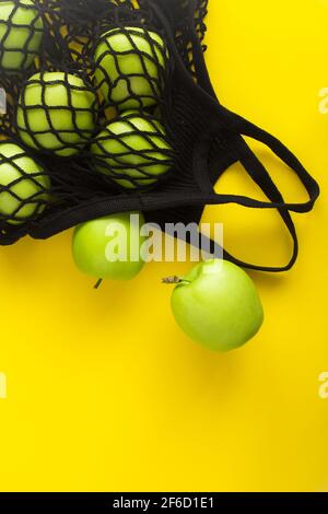 Nessun concetto di sacchetto di plastica. Borsa nera di shopping in mesh con mele verdi su sfondo giallo. Vista dall'alto. Spazio di copia. Foto Stock