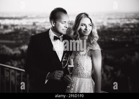 Le coppie di nozze si ergono sullo sfondo della città e bevono champagne da wineglass. Immagine in bianco e nero Foto Stock