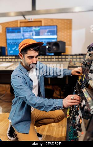 Foto d'inventario dell'hipster man utilizzando il pannello di controllo in studio di musica professionale. Foto Stock