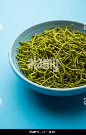 Gli spinaci o il palak SEV sono noodle salate fritte croccanti. Shev o namkeen verde spesso e sottile fatto in casa è un classico spuntino indiano. Servito in una ciotola o in un pl Foto Stock