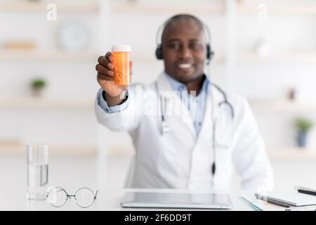 Trattamento farmacologico. Amichevole medico afroamericano che tiene il vaso di medicine e consiglia al paziente, allungandosi alla macchina fotografica Foto Stock