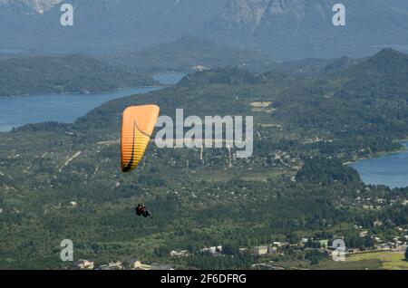 parapendio giallo sulla città di bariloche, in volo dalla collina otto al lago nahuel huapi Foto Stock