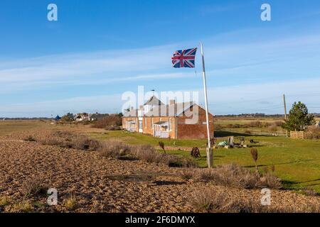 Case sulla spiaggia frazione costiera di Shingle Street, Hollesley Bay, Suffolk, Inghilterra, Regno Unito Union Jack bandiera battenti Foto Stock