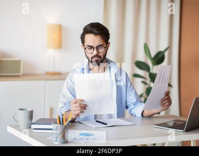 Bell'imprenditore orientale che legge i documenti finanziari mentre si siede alla scrivania In ufficio Foto Stock