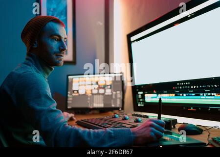 Attraente Male Video Editor funziona con filmati o video sul suo Personal computer, lavora in Creative Office Studio o a casa. Luci al neon Foto Stock