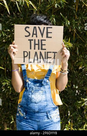 Ritratto di donna che ricopre il suo volto con una bandiera con lo slogan Save the Planet. È all'aperto in natura. Foto Stock