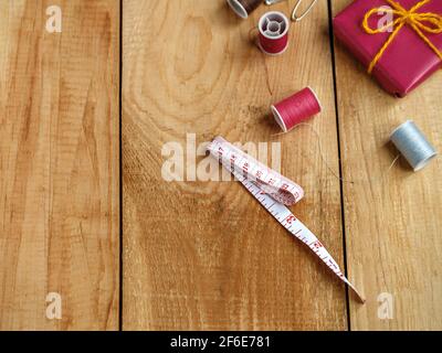 Nastro di misurazione del sarto, bobine di filo e scatola regalo rossa su tavole di legno marroni. Foto Stock