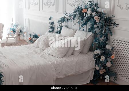 Camera da letto bianca. Il grande e confortevole letto matrimoniale è decorato con foglie e fiori magenta. Camera da letto in colori chiari e tenui. Letto di sposi novelli Foto Stock