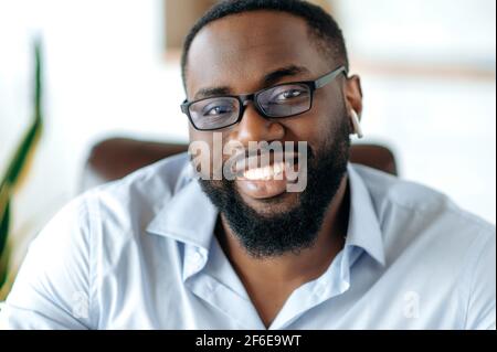 Primo piano ritratto di un bel amichevole afroamericano intelligente uomo in formale camicia blu e occhiali, imprenditore, agente o avvocato guardando e sorridendo alla fotocamera Foto Stock