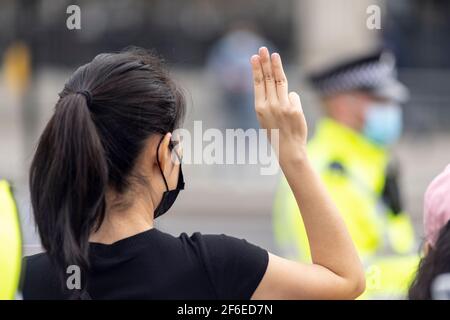 Londra, Regno Unito. 31 Marzo 2021. Un protettore fa il saluto a tre dita della resistenza di fronte a un ufficiale di polizia di passaggio in Piazza del Parlamento. I manifestanti si sono riuniti in Piazza del Parlamento - indossando maschere facciali e osservando le distanze sociali - prima di marciare all'ambasciata cinese in solidarietà con il popolo del Myanmar contro il colpo di stato militare e le uccisioni di civili. I discorsi sono stati fatti fuori dall'ambasciata. Dall'inizio del colpo di stato militare del 1° febbraio, oltre 520 persone sono state uccise in Myanmar dalle forze di sicurezza. Sabato scorso è stato il giorno più violento quando più di Foto Stock