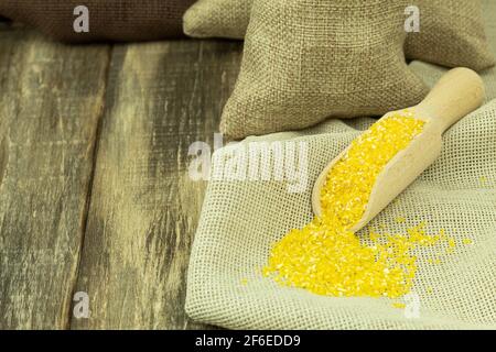 Il mais groats in un cucchiaio di legno. Granoturco grits con spazio per il testo e la pubblicità. Legno di fondo Foto Stock