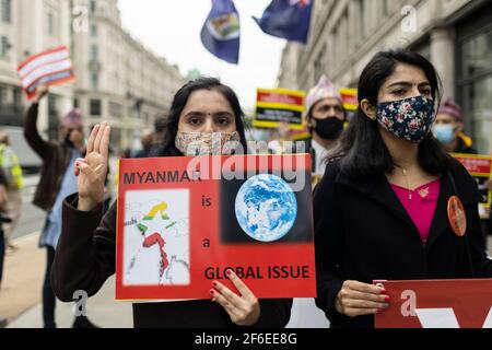 Londra, Regno Unito. 31 Marzo 2021. Un manifestante in marcia fa il saluto a tre dita della resistenza e tiene un cartello con la lettura 'yanmar è una questione globale'. I manifestanti si sono riuniti in Piazza del Parlamento - indossando maschere facciali e osservando le distanze sociali - prima di marciare all'ambasciata cinese in solidarietà con il popolo del Myanmar contro il colpo di stato militare e le uccisioni di civili. I discorsi sono stati fatti fuori dall'ambasciata. Dall'inizio del colpo di stato militare del 1° febbraio, oltre 520 persone sono state uccise in Myanmar dalle forze di sicurezza. Sabato scorso è stato il giorno più violento quando mo Foto Stock