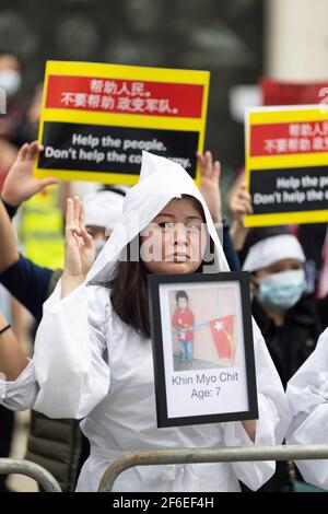 Londra, Regno Unito. 31 Marzo 2021. Una donna protesteria vestita di bianco rende il saluto a tre dita della resistenza e tiene una fotografia di una vittima deceduta fuori dell'ambasciata cinese. I manifestanti si sono riuniti in Piazza del Parlamento - indossando maschere facciali e osservando le distanze sociali - prima di marciare all'ambasciata cinese in solidarietà con il popolo del Myanmar contro il colpo di stato militare e le uccisioni di civili. I discorsi sono stati fatti fuori dall'ambasciata. Dall'inizio del colpo di stato militare del 1° febbraio, oltre 520 persone sono state uccise in Myanmar dalle forze di sicurezza. Sabato scorso w Foto Stock