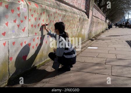 I cuori rossi che formano il National Covid Memorial Wall, un tributo alle oltre 150,000 vittime britanniche della pandemia di Coronavirus. La famiglia e gli amici delle vittime di Covid-19 hanno iniziato a lavorare sul muro situato fuori dall'ospedale St Thomas, e che si affaccia alla Camera del Parlamento a Westminster, il 30 marzo 2021, a Londra, Inghilterra. Lo scorso anno il primo Ministro Boris Johnson è stato trattato per Covid a St Thomas. Foto Stock