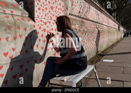 I cuori rossi che formano il National Covid Memorial Wall, un tributo alle oltre 150,000 vittime britanniche della pandemia di Coronavirus. La famiglia e gli amici delle vittime di Covid-19 hanno iniziato a lavorare sul muro situato fuori dall'ospedale St Thomas, e che si affaccia alla Camera del Parlamento a Westminster, il 30 marzo 2021, a Londra, Inghilterra. Lo scorso anno il primo Ministro Boris Johnson è stato trattato per Covid a St Thomas. Foto Stock