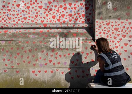 I cuori rossi che formano il National Covid Memorial Wall, un tributo alle oltre 150,000 vittime britanniche della pandemia di Coronavirus. La famiglia e gli amici delle vittime di Covid-19 hanno iniziato a lavorare sul muro situato fuori dall'ospedale St Thomas, e che si affaccia alla Camera del Parlamento a Westminster, il 30 marzo 2021, a Londra, Inghilterra. Lo scorso anno il primo Ministro Boris Johnson è stato trattato per Covid a St Thomas. Foto Stock