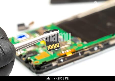 Il tecnico può tenere una scheda microSD con pinzette in una riparare il centro di assistenza davanti a una chiusura dello smartphone smontata su Foto Stock