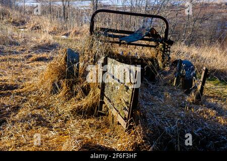 Un vecchio spanditore di concime derelict si siede rotto giù e coperto in erba secca, lichene e muschio. L'attrezzatura agricola vintage, trainata da cavalli, presenta una vecchia ruggine Foto Stock