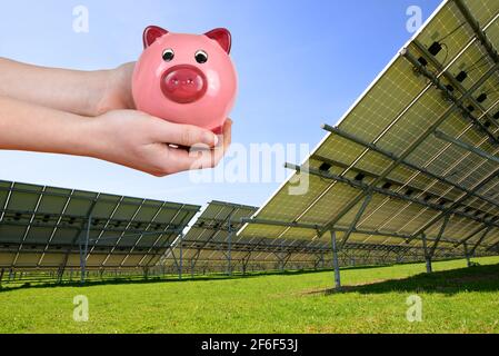 Pannelli solari e banca piggy in hands.Concept di risparmio di denaro per l'energia. Foto Stock