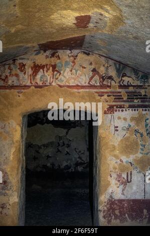 Due cavalieri etruschi ritornano da una spedizione di caccia con i loro servi che trasportano la loro cattura e i loro cani che corrono accanto ai cavalli. Affresco sul timpano della prima camera di una tomba etrusca di 2.500 anni, la Tomba di caccia e pesca, nella necropoli di Monterozzi dell'antica città di Tarchuna o Tarchna, ora Tarquinia, Lazio, Italia. Foto Stock