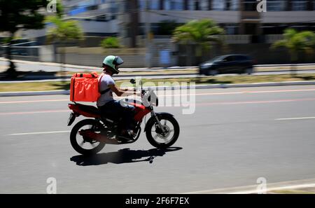 salvador, bahia, brasile - 6 gennaio 2021: L'uomo che consegna il cibo da applicazione è visto che cavalcano una motocicletta sulla strada nel quartiere di Pituba in th Foto Stock