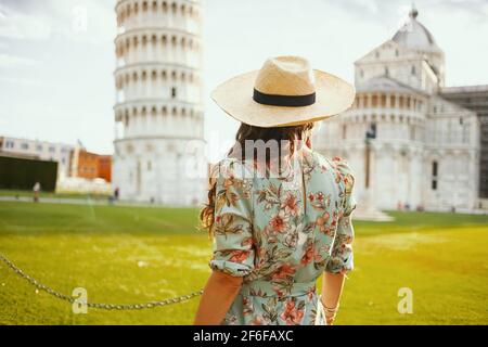 Visto da una donna viaggiatore in abito floreale con cappello turistico vicino alla Torre Pendente a Pisa, Italia. Foto Stock