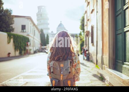 Visto da dietro donna turistica in abito floreale con zaino che ha un tour a piedi a Pisa, Italia. Foto Stock