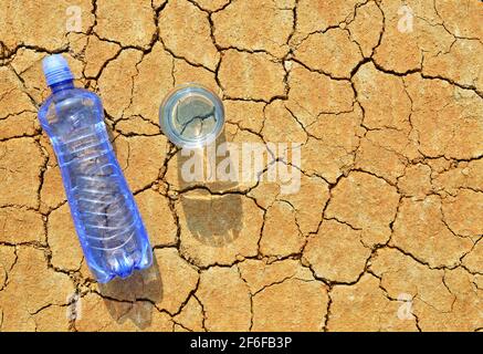 Bottiglia e bicchiere d'acqua su terreno asciutto e incrinato. Concetto di riscaldamento globale. Foto Stock