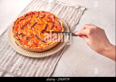 Tagli a mano della donna con un coltello torta di quiche fatte in casa con pollo, pomodori secchi, formaggio cheddar su piatto di ceramica Foto Stock