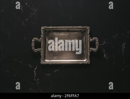 Disposizione piatta di un vassoio vuoto in argento antico contro il buio marmo Foto Stock