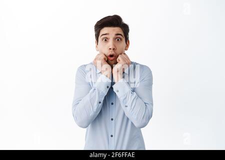 Immagine di un uomo d'affari sorpreso ed eccitato dicono WOW, gasting e guardando affascinato alla macchina fotografica, impressionato da promo Deal, in piedi contro bianco Foto Stock