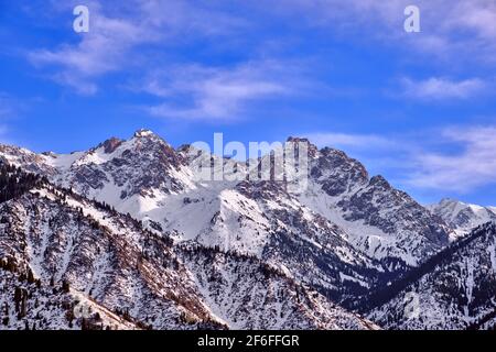 Maestose vette rocciose con foresta di abeti contro un cielo blu con nuvole nella stagione invernale Foto Stock