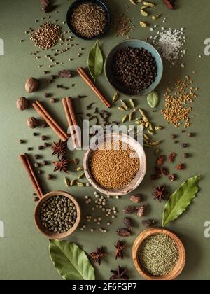 Varie spezie secche in piccole ciotole e sparse su sfondo verde. Vista dall'alto Foto Stock