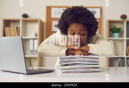 Lavoratrice d'ufficio afroamericana che dorme sulla pila di documenti di carta alla scrivania Foto Stock