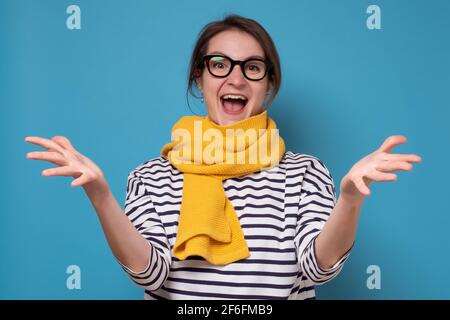 donna in occhiali e sciarpa gialla eccitata in piedi con bocca aperta e palmi aperte Foto Stock
