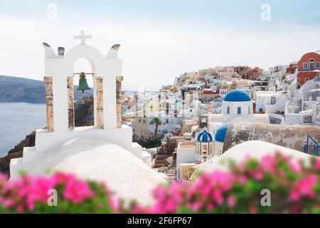 Oia villaggio attraverso fiori e tradizionale greco arco chiesa bianca con croce e campane nel villaggio di Oia delle Cicladi, Santorini Foto Stock
