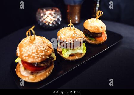 Tre mini hamburger su un supporto allungato rettangolare nero. Foto Stock