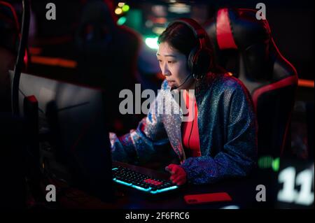 Un giovane giocatore cinese di eSport in un torneo internazionale di eSport. Un cyber team multirazziale sta giocando un gioco di sparatutto online. Luce al neon Foto Stock