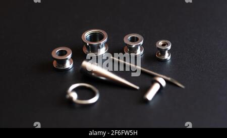 Set per piercing su sfondo scuro, tunnel auricolare, tunnel e orecchini per le orecchie e la lingua. Foto Stock