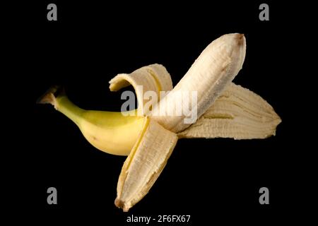 Una banana matura, sbucciata a metà, su fondo nero, isolata Foto Stock