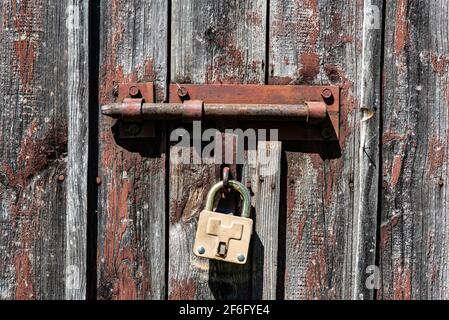 Vecchia porta in legno arrugginita arrugginita con serratura e lucchetto. Primo piano della serratura vintage arrugginita sulla porta chiusa Foto Stock