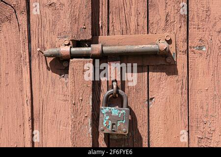 Vecchia porta in legno arrugginita arrugginita con serratura e lucchetto. Primo piano della serratura vintage arrugginita sulla porta chiusa Foto Stock