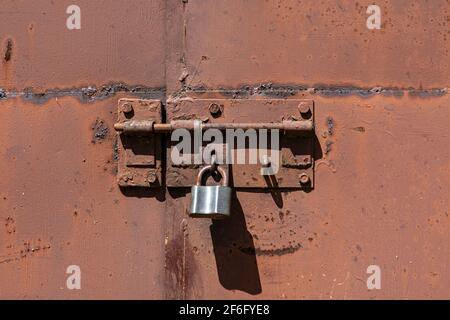 Vecchia porta in metallo arrugginita arrugginita con serratura e lucchetto. Primo piano della serratura vintage arrugginita sulla porta chiusa Foto Stock
