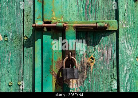 Vecchia porta in legno arrugginita arrugginita con serratura e lucchetto. Primo piano della serratura vintage arrugginita sulla porta chiusa Foto Stock